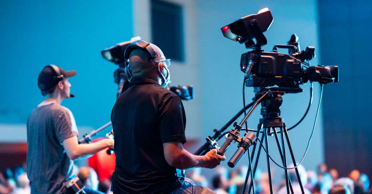Two cameramen operate professional video cameras at an indoor event.